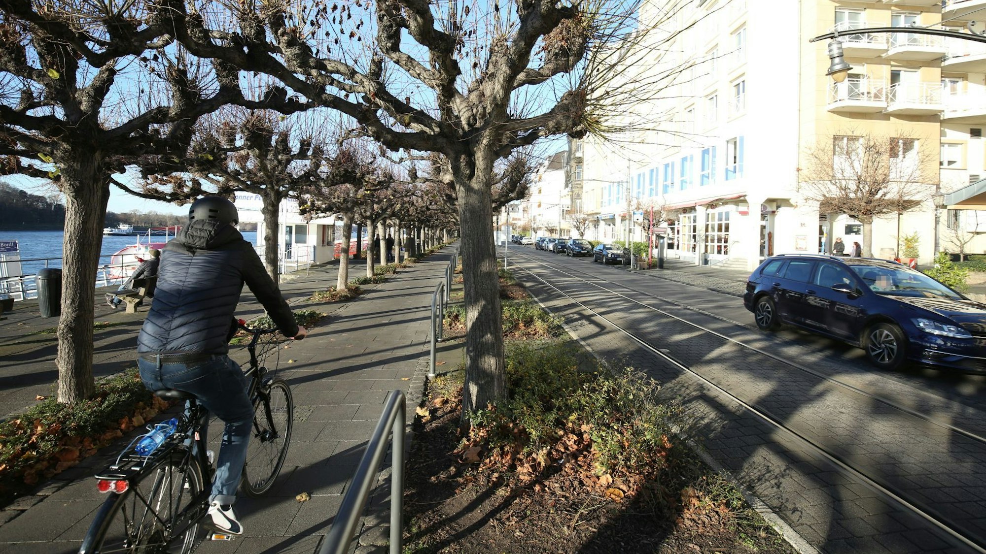 Ein Radfahrer fährt in der Altstadt von Königswinter an der Rheinpromenade entlang. Rechts daneben fährt ein blaues Auto über die Rheinallee.