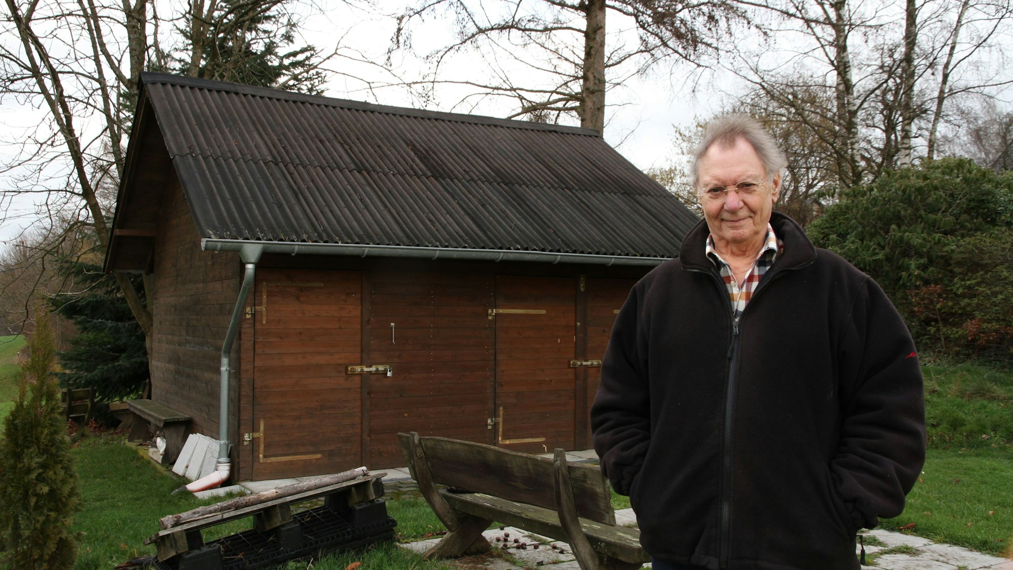 Ein Mann steht vor einem massiven Gartenhäuschen aus Holz.