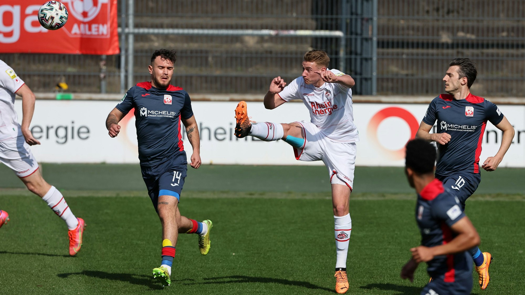 Ein Fußballspieler wird von zwei Gegnern bedrängt und schießt den Ball weg.