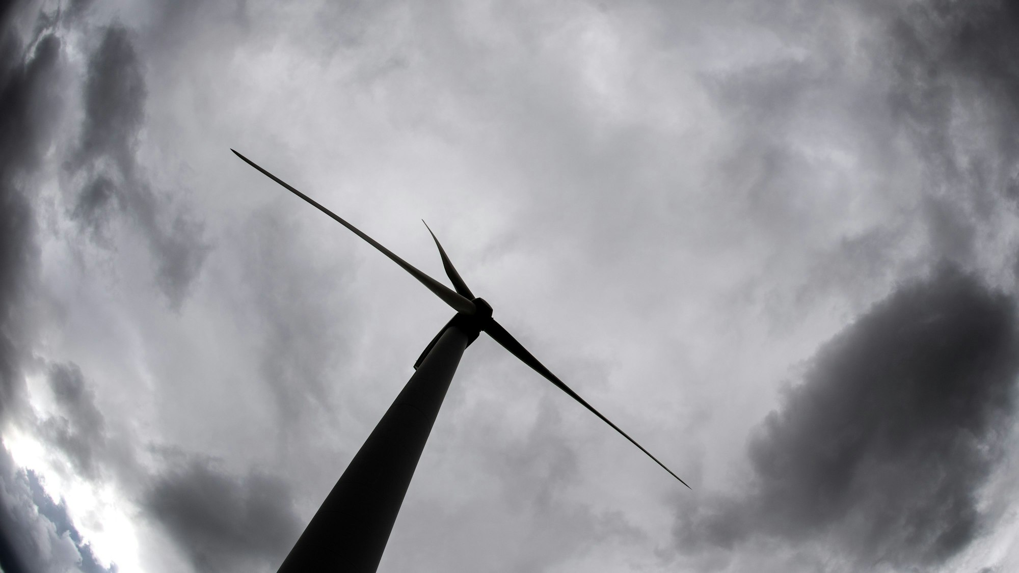 Ein Windrad ragt in den mit Wolken verhangenen Himmel.