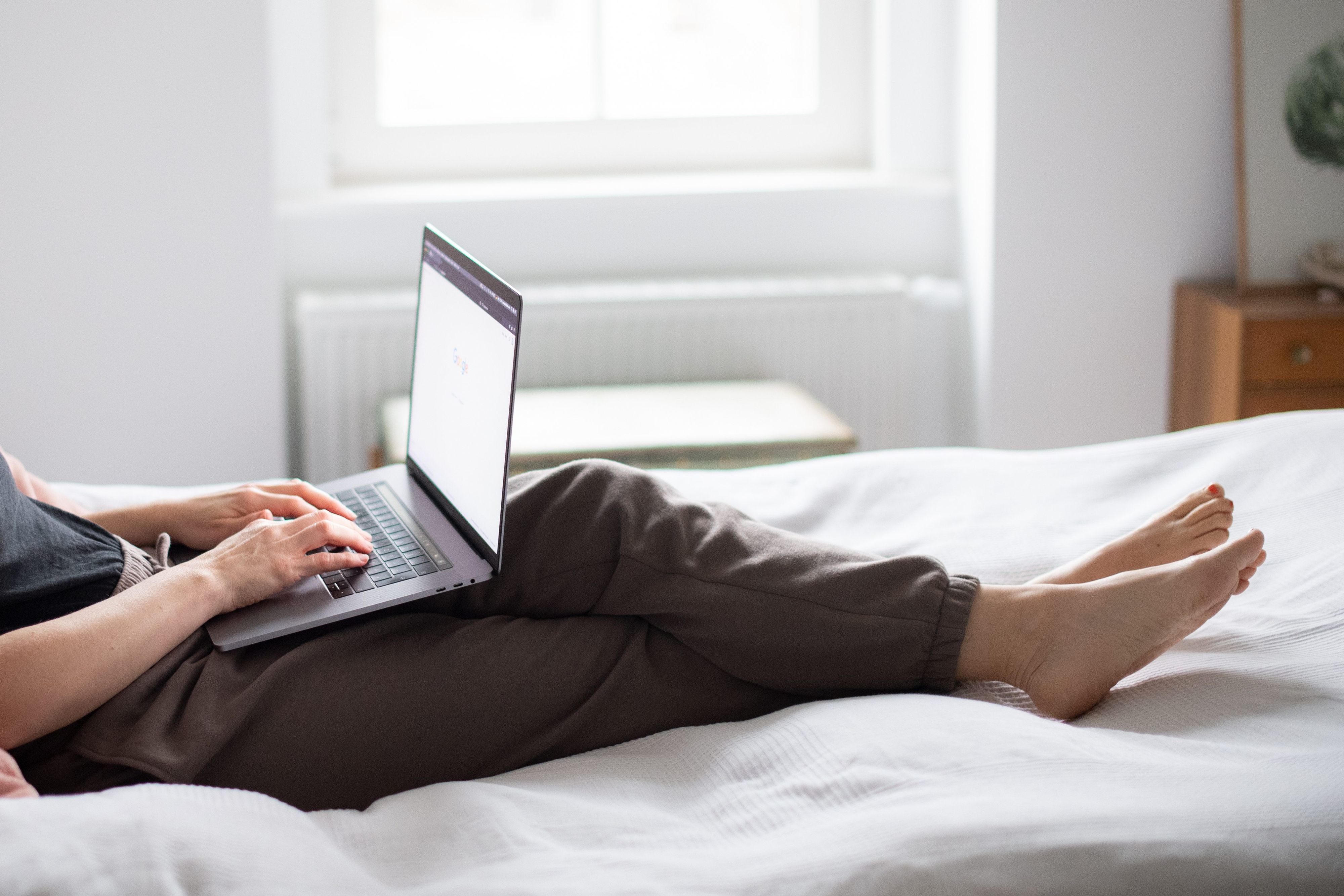 Eine Person liegt auf einem Bett und tippt am Laptop.