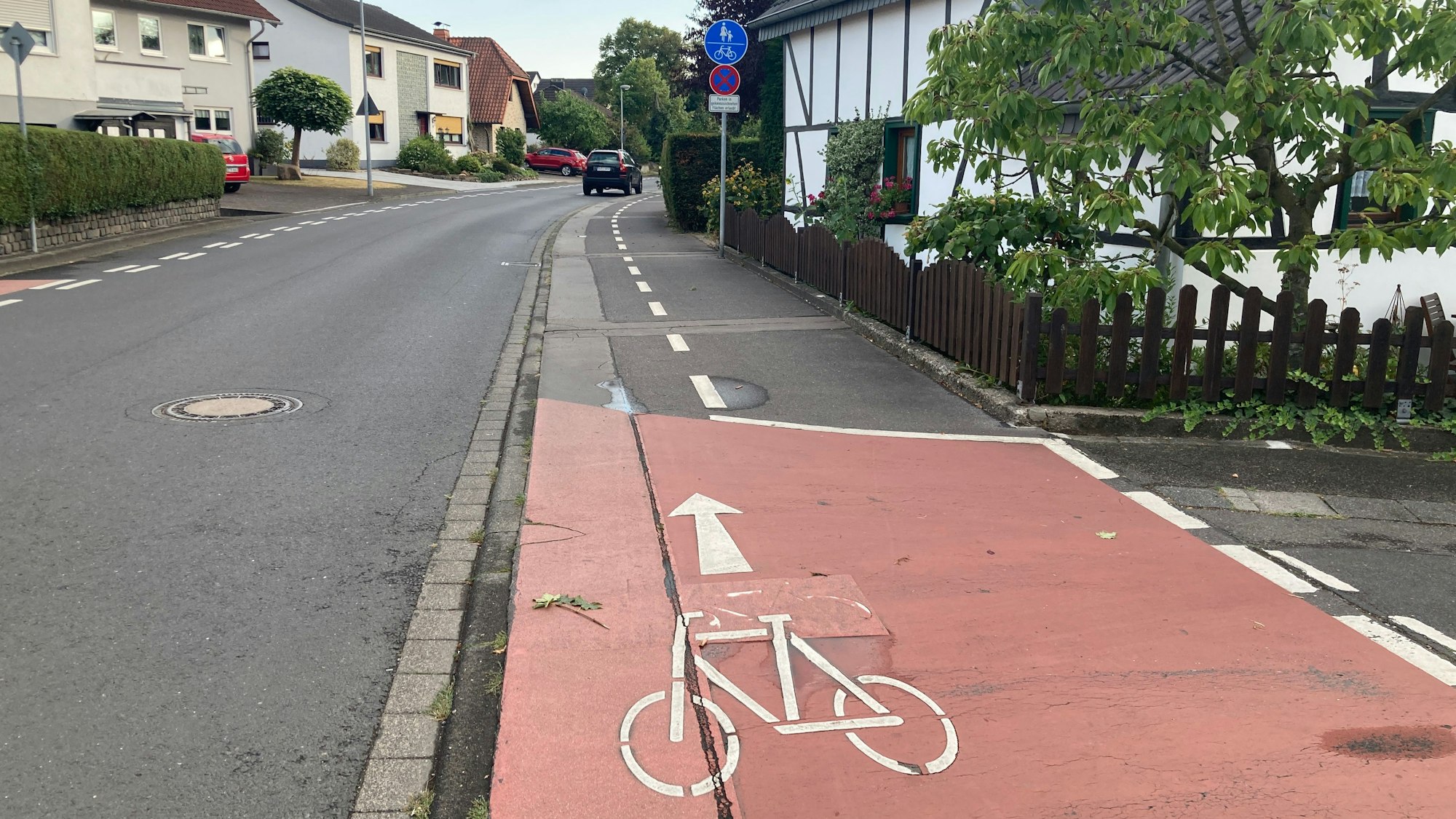 Über eine Kreuzung ist eine rote Markierung für einen Fahrradweg, dahiner folgt ein geteilter Fuß- und Radweg, auf dem auch Autos parken.