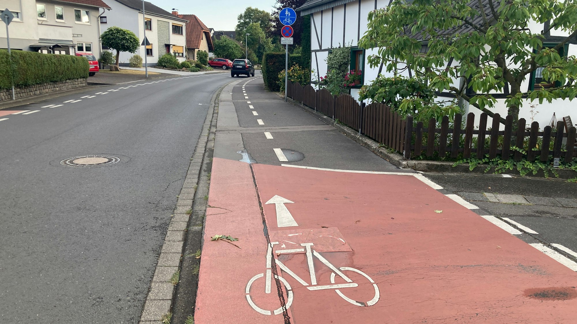 Bachstraße in Lohmar. Ein Fahrradweg ist rechts von der Straße zu sehen. Im Hintergrund stehen Häuser und Autos.