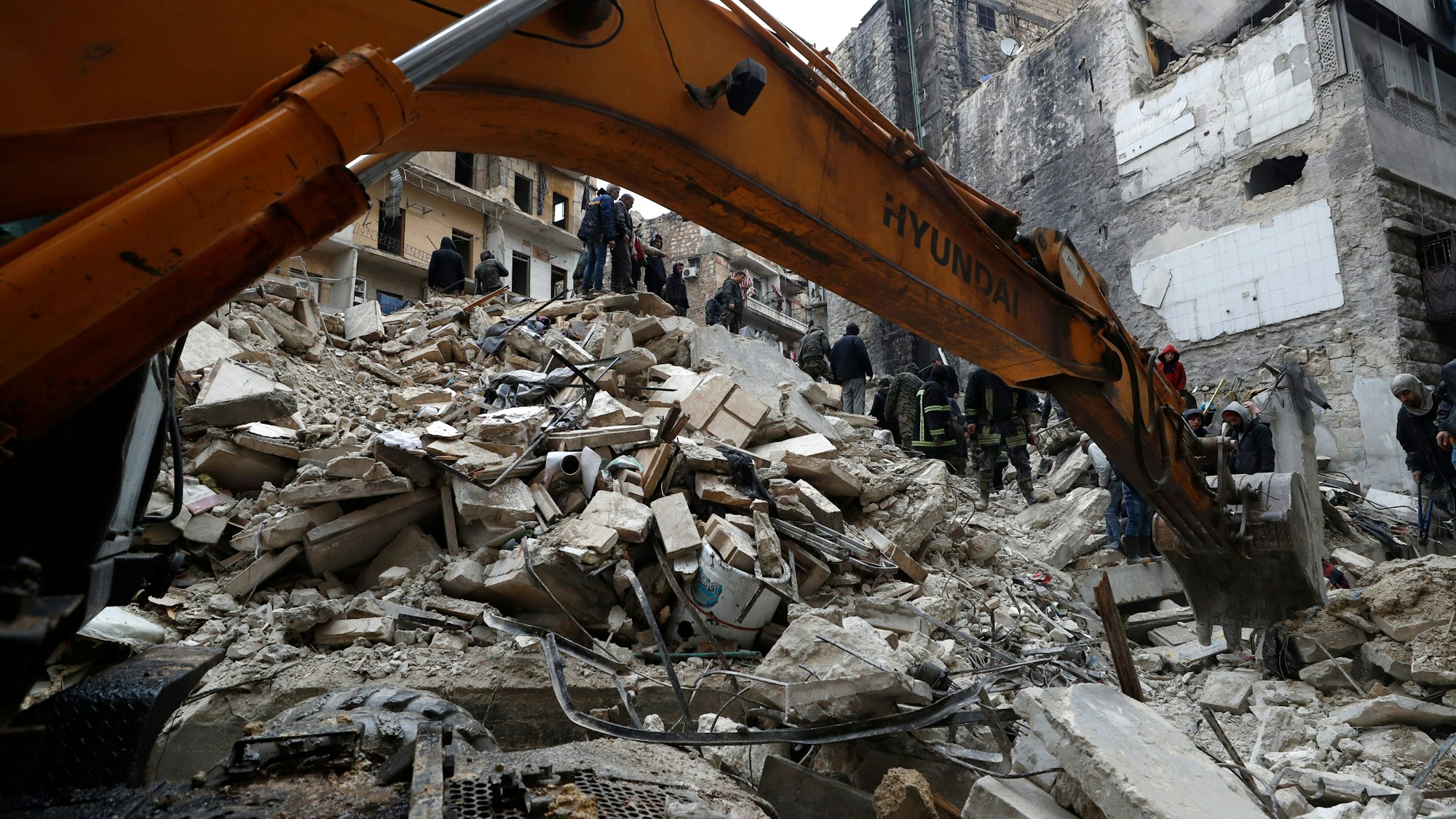 Mitarbeiter des syrischen Zivilschutzes und Sicherheitskräfte durchsuchen die Trümmer eingestürzter Gebäude.