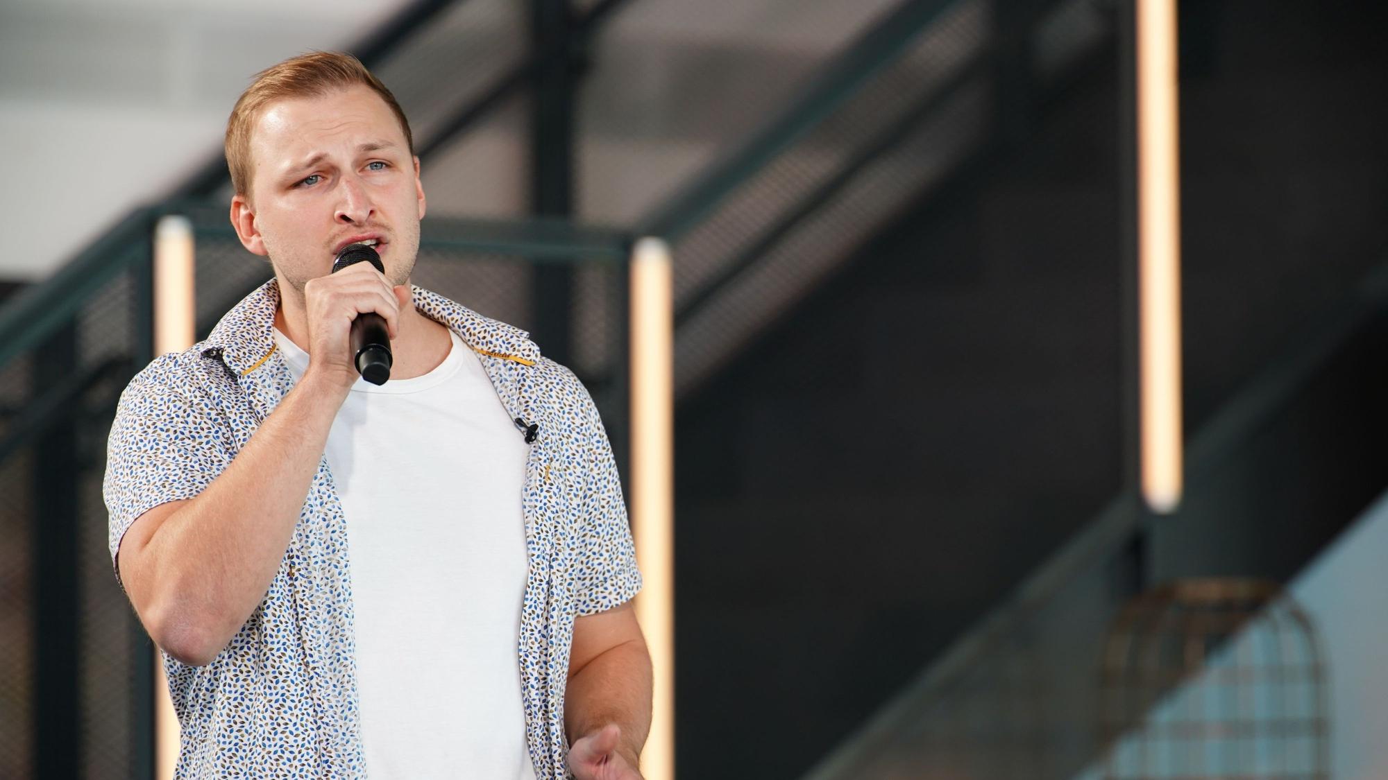 David steht auf einer Bühne und singt in ein Mikro.