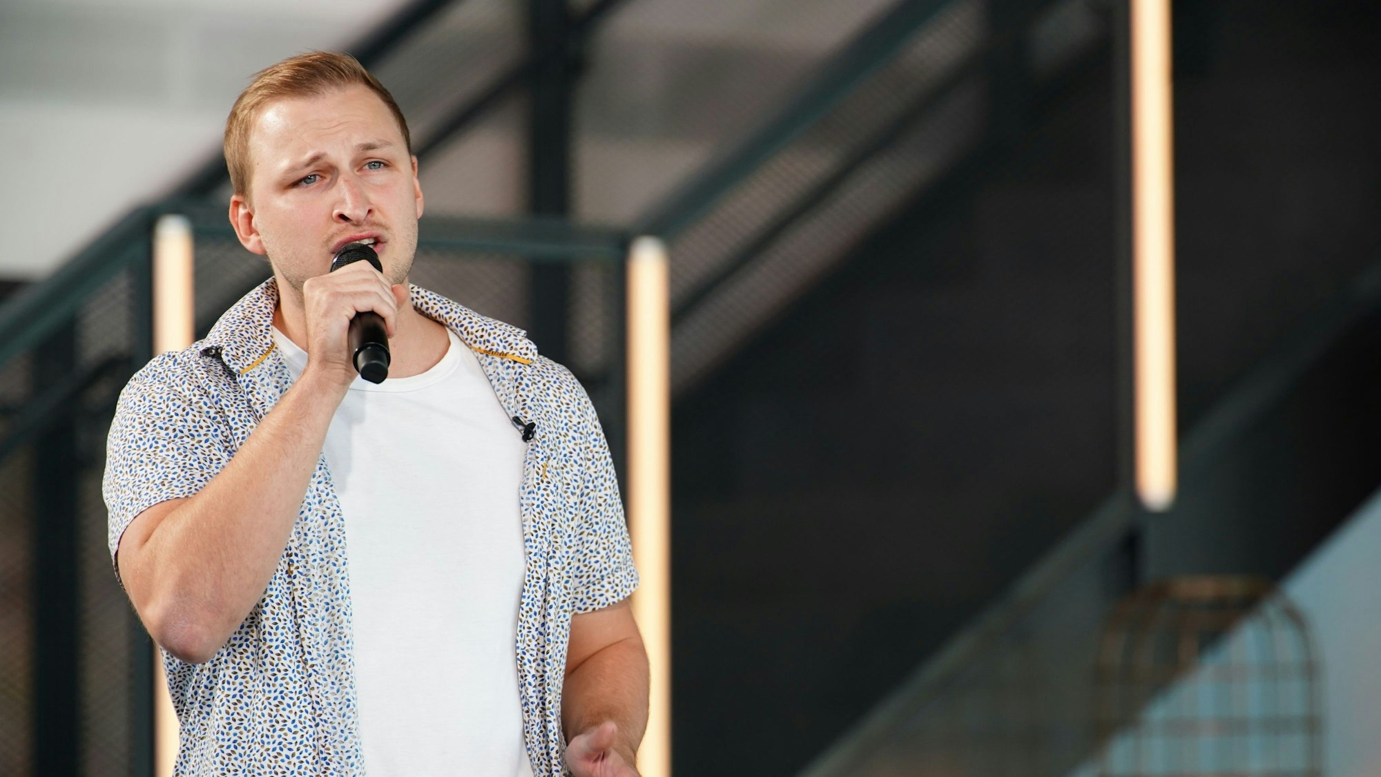 David steht auf einer Bühne und singt in ein Mikro.