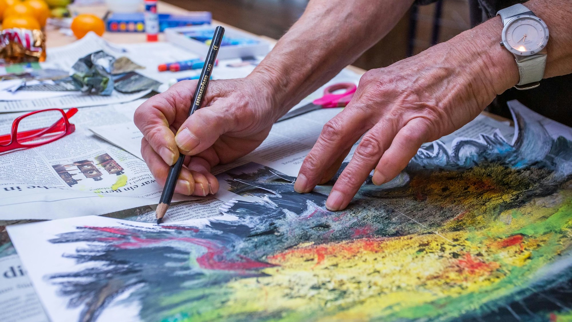 Zwei ältere Hände malen ein Bild, das mit Zeitungspapier unterlegt ist