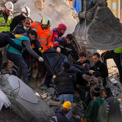 07.02.2023, Türkei, Adana: Mitglieder eines Rettungsteams tragen den Körper einer Person, die in den Trümmern eines zerstörten Gebäudes gefunden wurde. Rettungskräfte suchen weiterhin nach Überlebenden in den Trümmern tausender Gebäude, die durch ein starkes Erdbeben und mehrere Nachbeben, die die Osttürkei und das benachbarte Syrien erschütterten, eingestürzt waren.