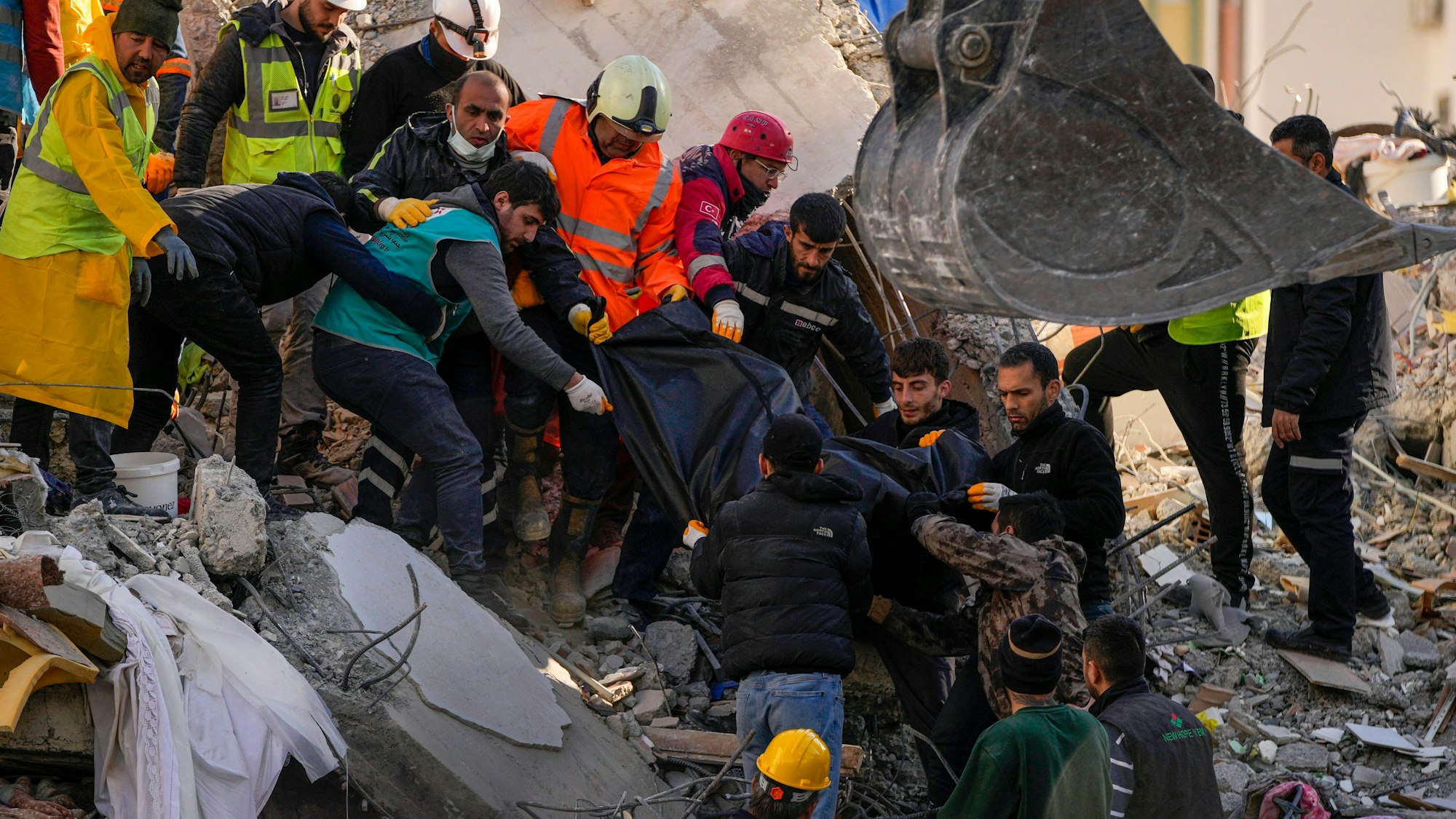 07.02.2023, Türkei, Adana: Mitglieder eines Rettungsteams tragen den Körper einer Person, die in den Trümmern eines zerstörten Gebäudes gefunden wurde. Rettungskräfte suchen weiterhin nach Überlebenden in den Trümmern tausender Gebäude, die durch ein starkes Erdbeben und mehrere Nachbeben, die die Osttürkei und das benachbarte Syrien erschütterten, eingestürzt waren.