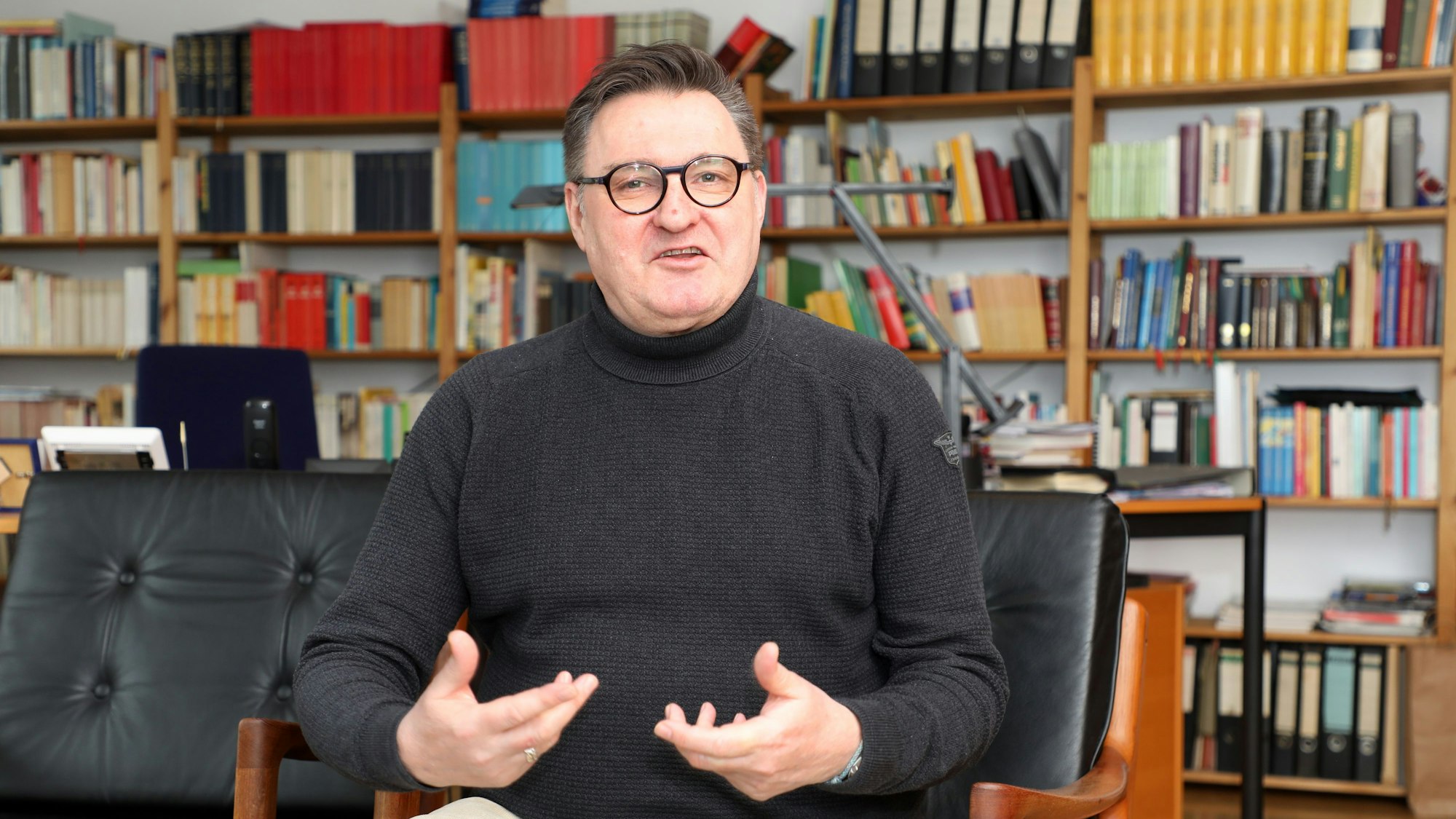 Kreisdechant Norbert Hörter sitzt vor einem Bücherregal in seinem Arbeitszimmer und spricht.