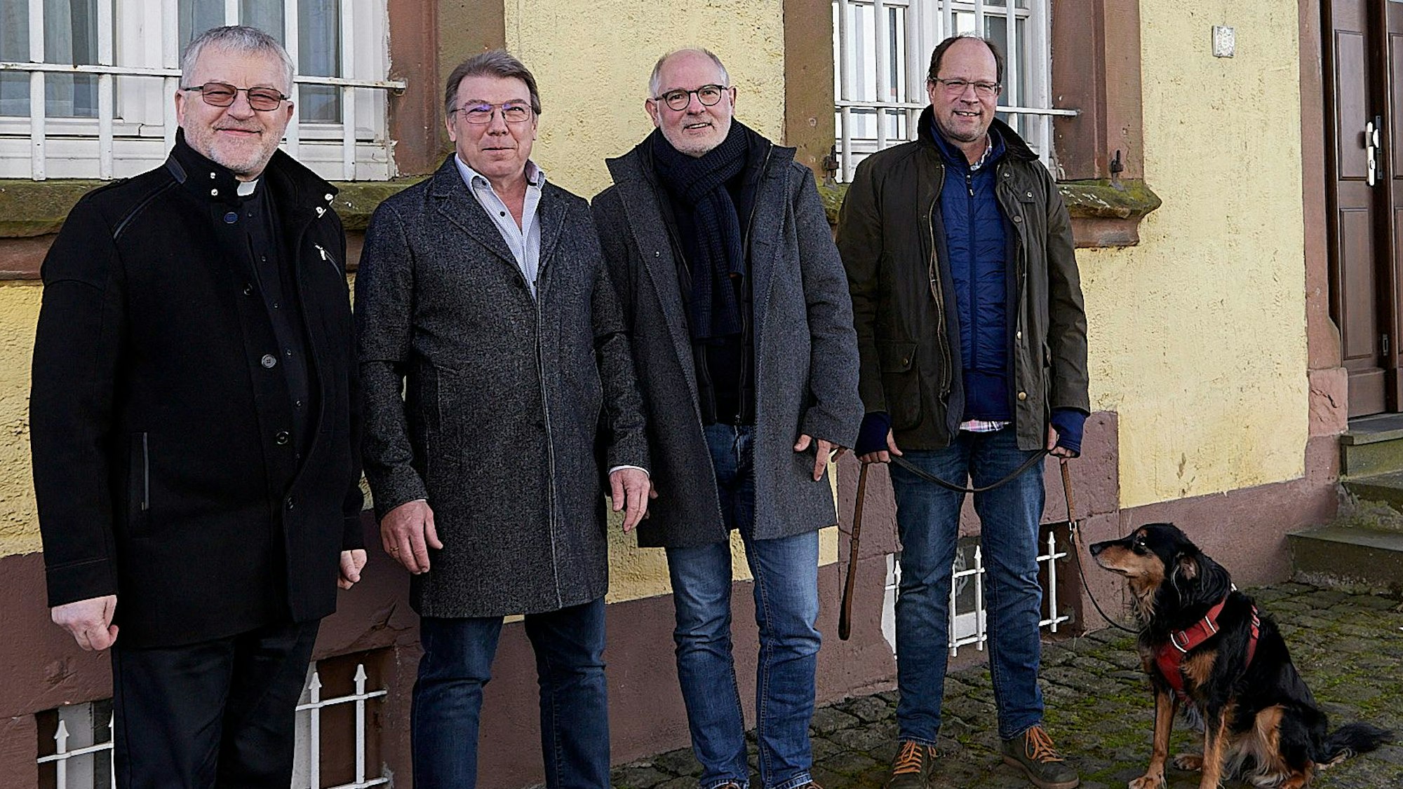 Vier Männer und ein Hund stehen vor einem Haus.