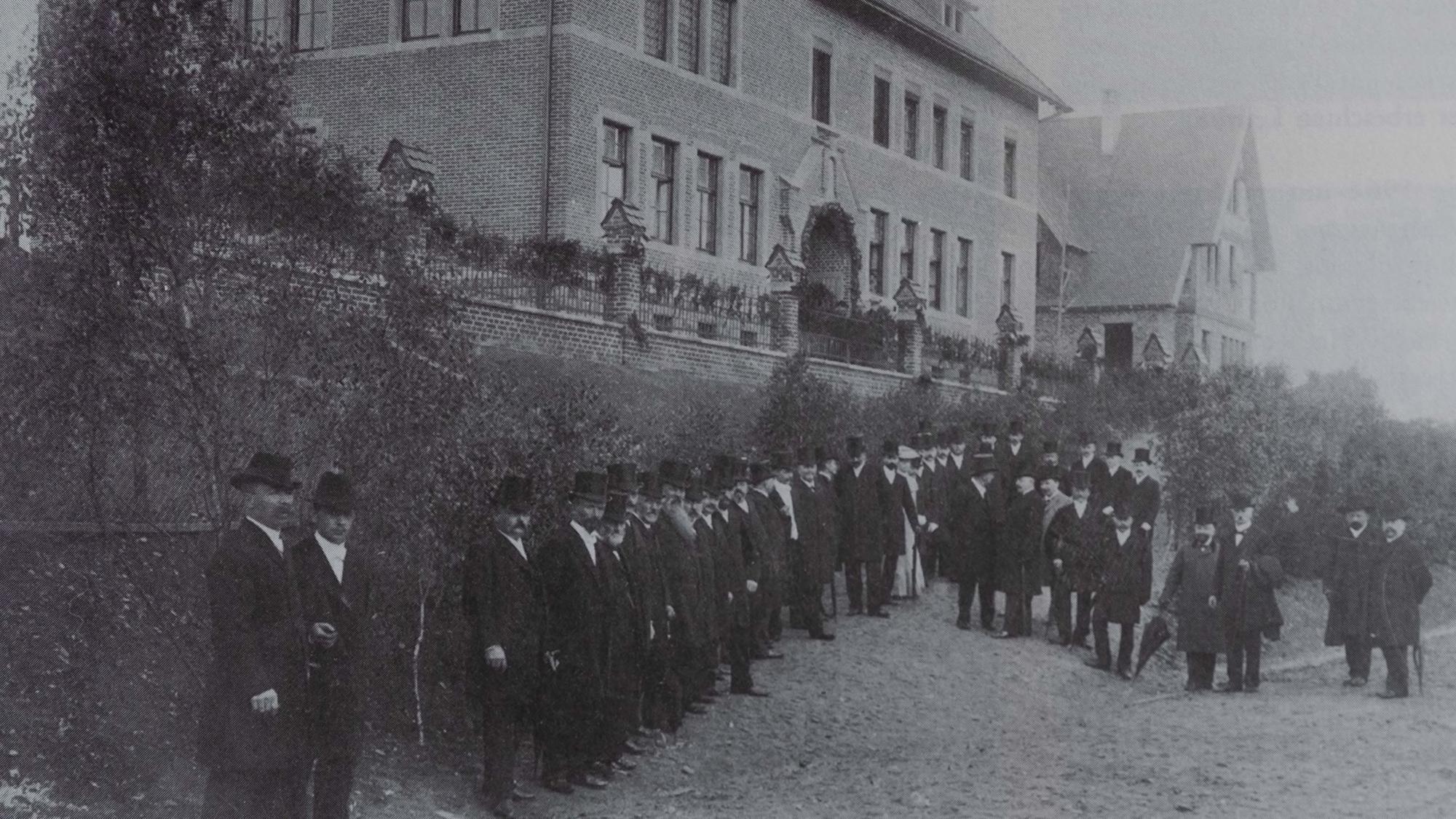 Zu sehen ist ein historisches Foto mit Männern in Frack und Zylinder.