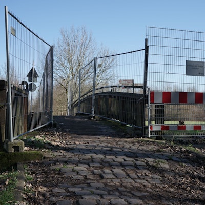 Man sieht eine schmale Brücke über ein Gewässer, welche an den Geländern durch Bauzäune begrenzt wird.