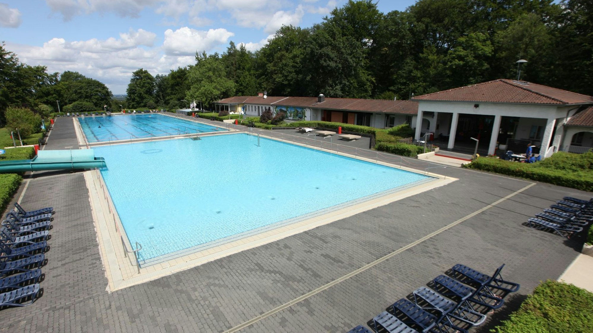 Zwei große Becken im Freibad, rechts flache Gebäude mit den Umkleiden und Duschen.