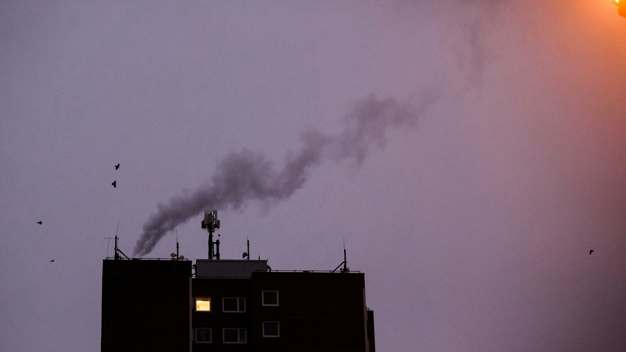 Nur in einer Wohnung eines Mehrfamilienhauses brennt am frühen Morgen Licht, während von einer Heizungsanlage Dampf aufsteigt. Die teils massiv gestiegenen Preise für Gas und Strom bereiten viele Menschen in Deutschland finanzielle Schwierigkeiten.