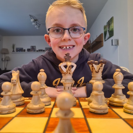 Nick sitzt hinter einem Schachbrett mit Figuren und schaut in die Kamera.