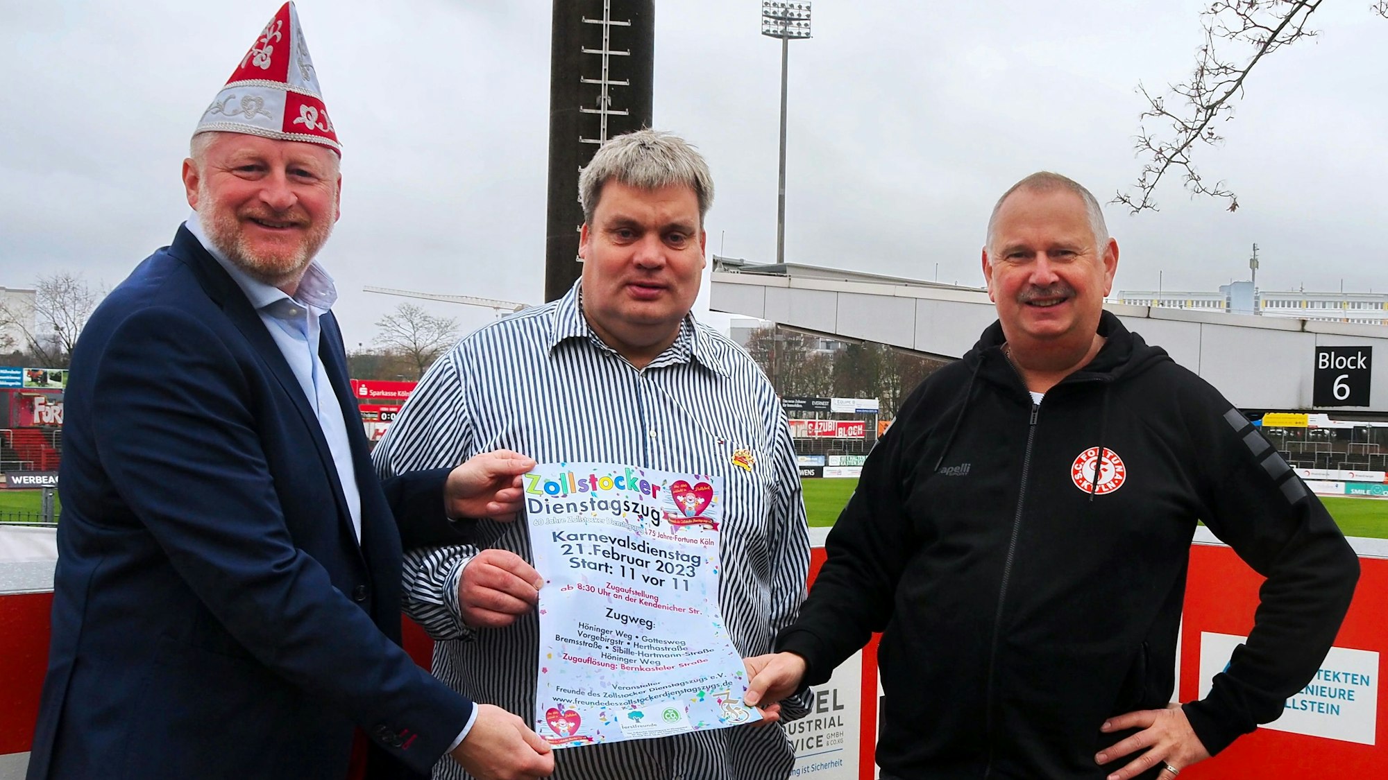 Stefan Puczynski, Michael Siegenbruck und Herbert Thelen stehen vor dem Stadion und halten ein Plakat des Zollstocker Dienstagszugs in die Kamera.