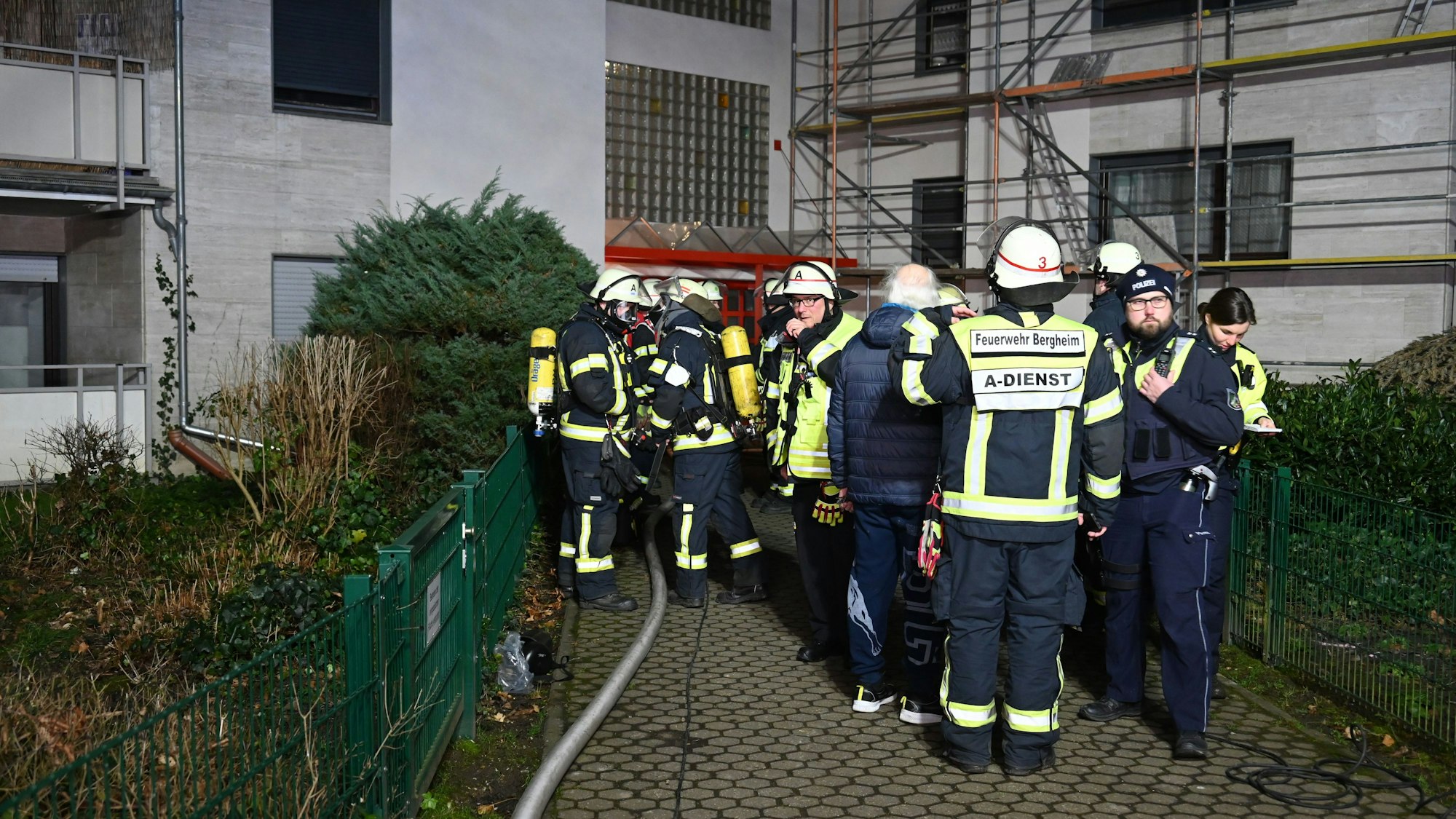 Einsatzkräfte der Feuerwehr Bergheim stehen vor dem Mehrfamilienhaus.
