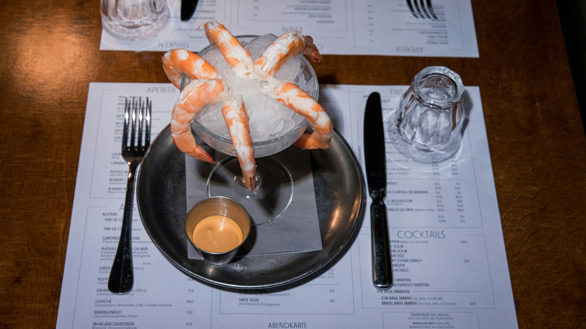 Garnelen auf Eiswürfeln in einem Glas, daneben ein Schälchen mit Cocktailsauce