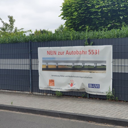 An einem Zaun in Niederkassel hängt ein Protest-Transparent gegen das Autobahn-Projekt Rheinspange 553.