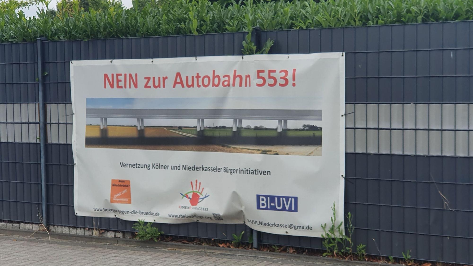 An einem Zaun in Niederkassel hängt ein Protest-Transparent gegen das Autobahn-Projekt Rheinspange 553.