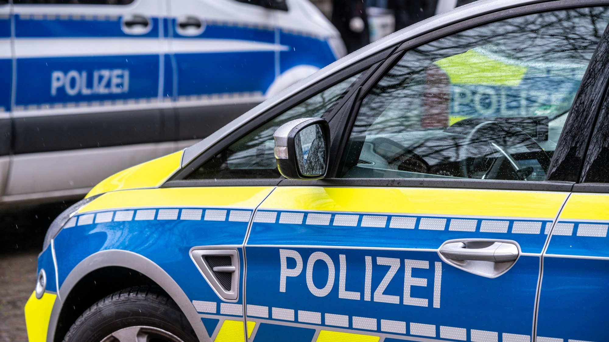 Auf dem Bild ist ein blau-gelbes Polizeifahrzeug zu sehen. Im Hintergrund sind weitere Polizeifahrzeuge.