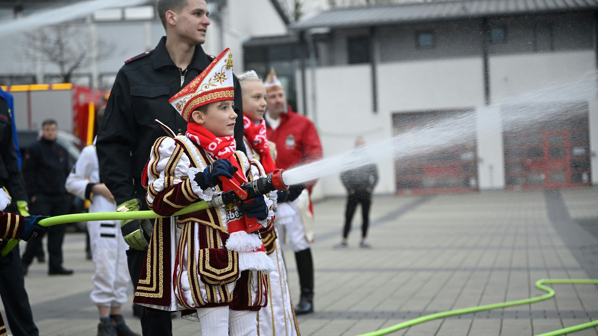 Ein Kinderprinz hält ein Feuerwehrstrahlrohr aus dem Wasser spritzt.
