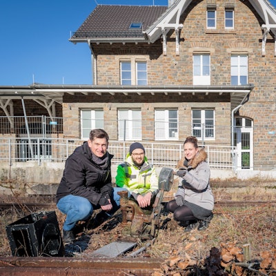 Drei Menschen knien vor dem alten Bahnhof in Morsbach.