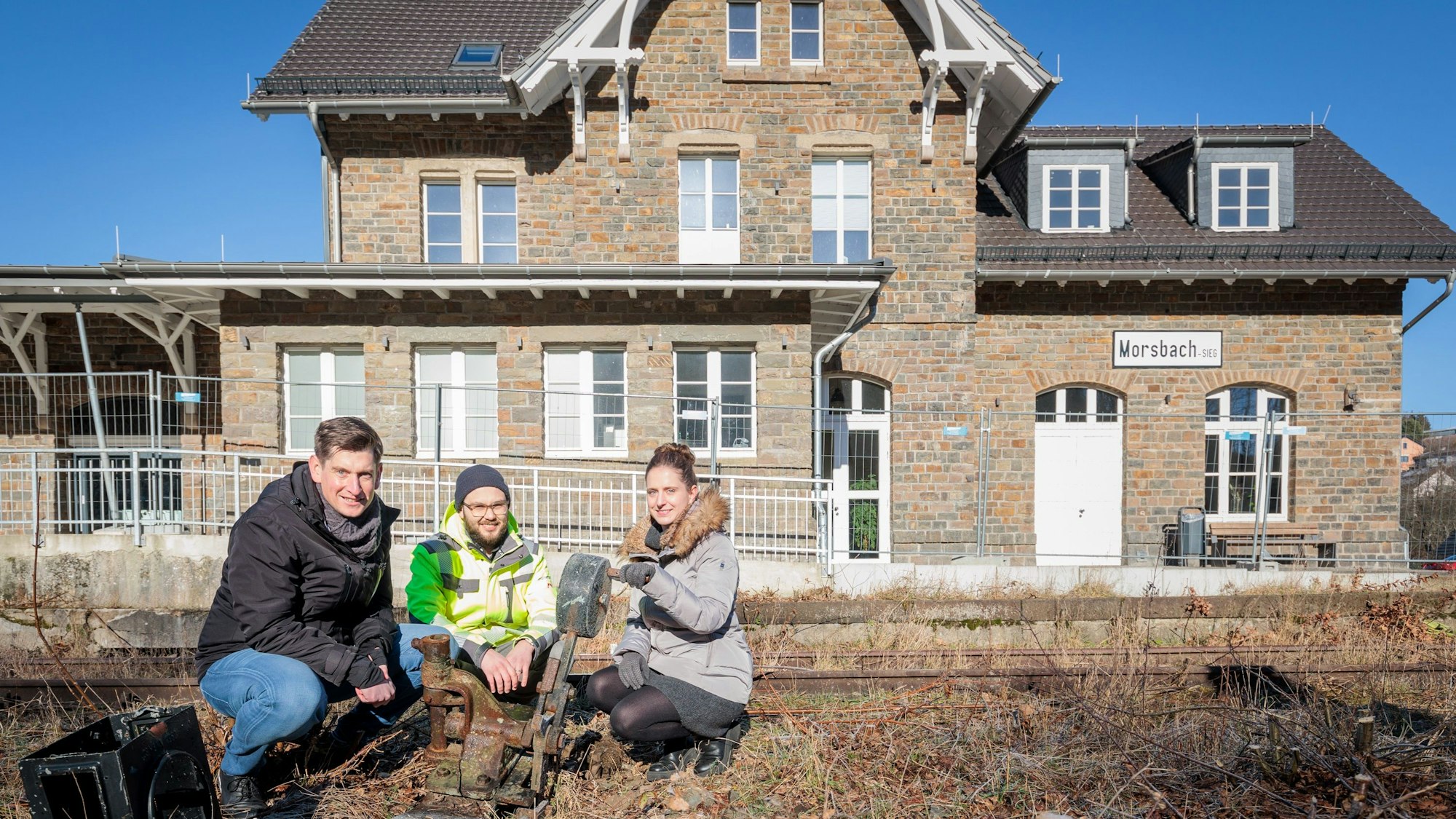 Drei Menschen knien vor dem alten Bahnhof in Morsbach.