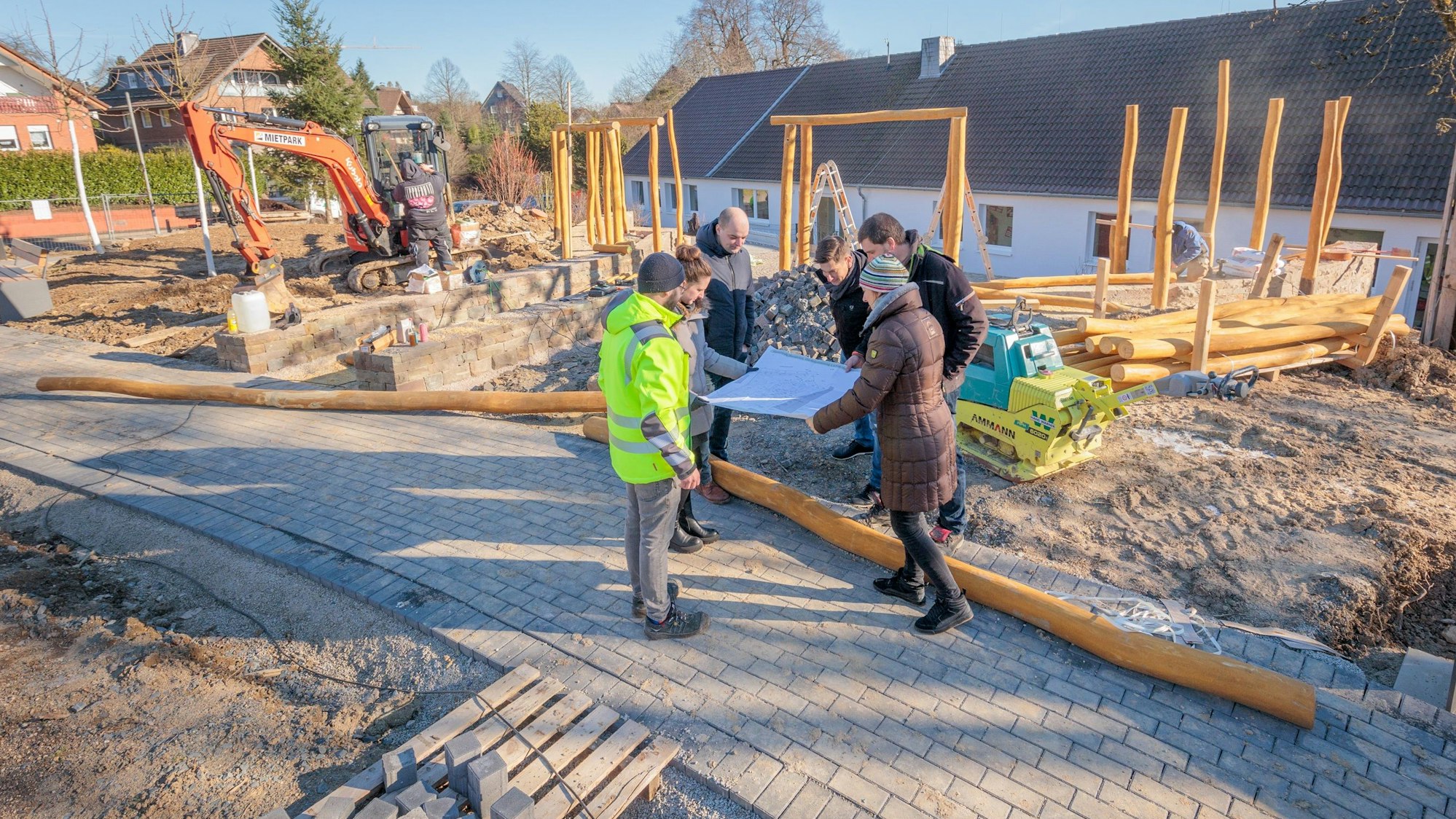 Sechs Menschen stehen um einen Plan inmitten des Baugebiets der Grünen Oase.