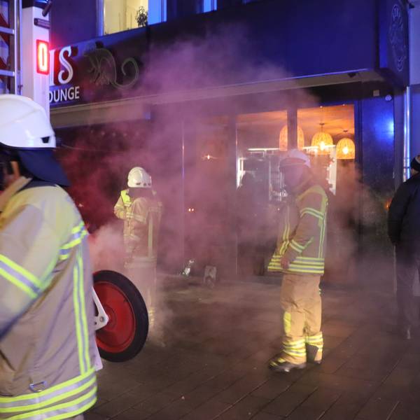 Feuerwehrleute stehen vor einem Gebäude, viel Rauch ist in der Luft.