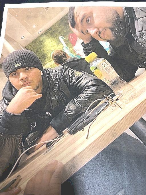 Zwei Männer mit dunkler Kleidung und dunklen Haaren sitzen an einem Tisch und stützen ihr Gesicht in ihre Hände.