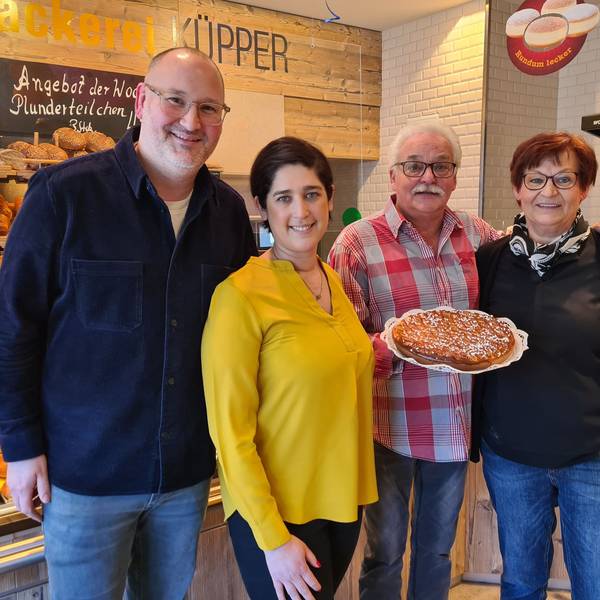 Vor einer Brottheke steht Familie Küpper. Ein Mann hält einen Kuchen in der Hand.
