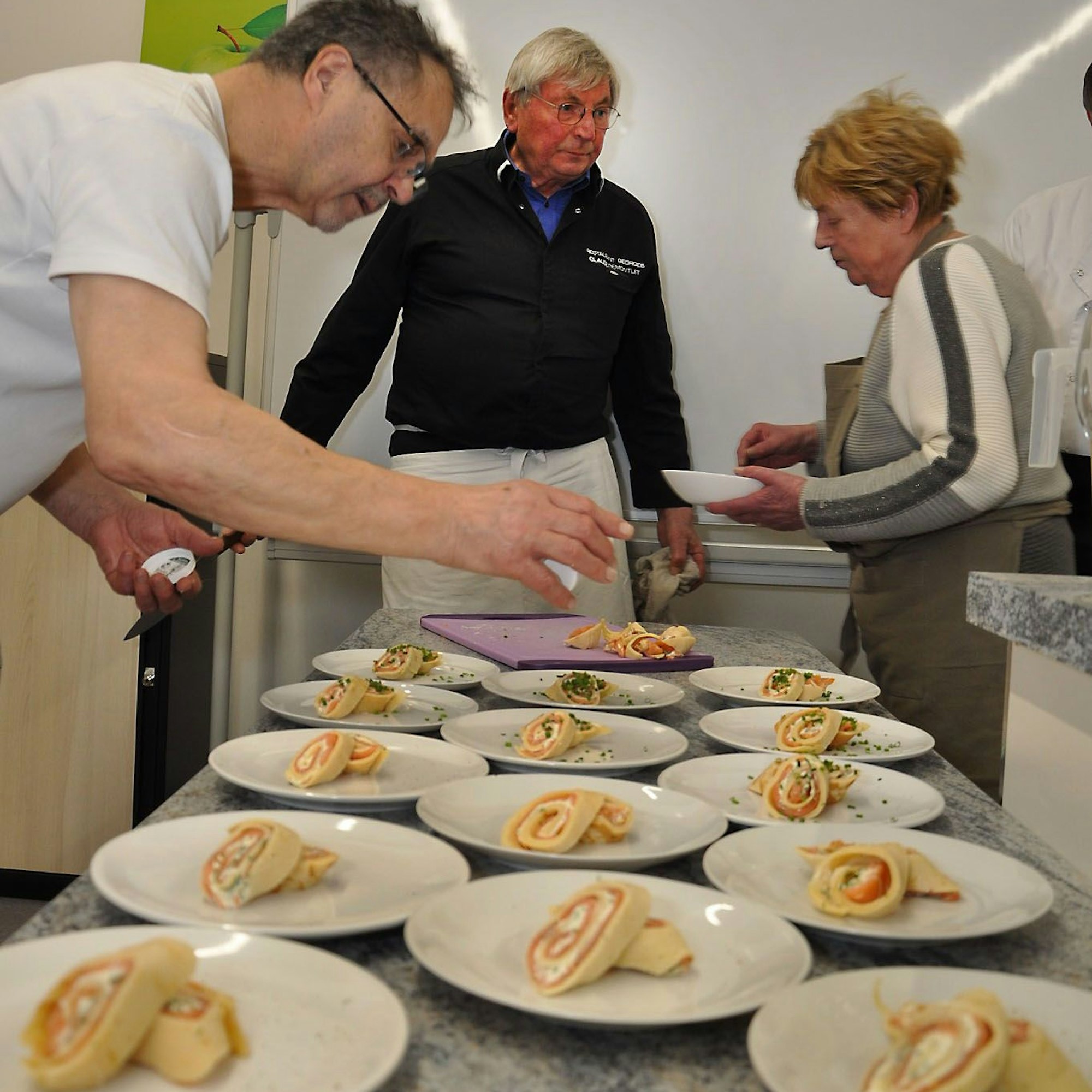 Zwei Köche und eine Köchin richten auf einem Tisch sorgfältig die Vorspeisenteller an.