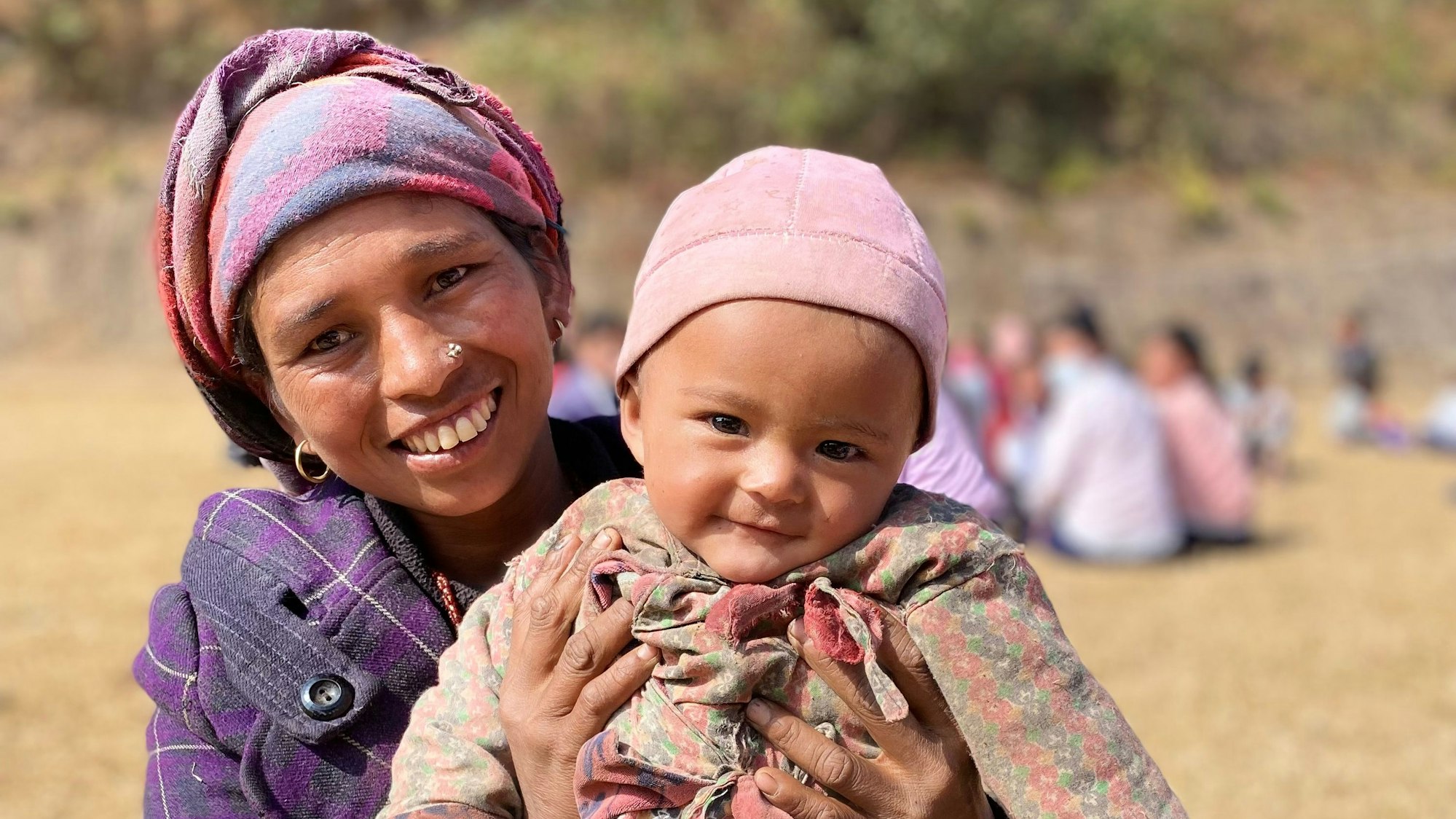 Eine Mutter hält ihr Kleinkind im Arm. Beide schauen und lachen in die Kamera.