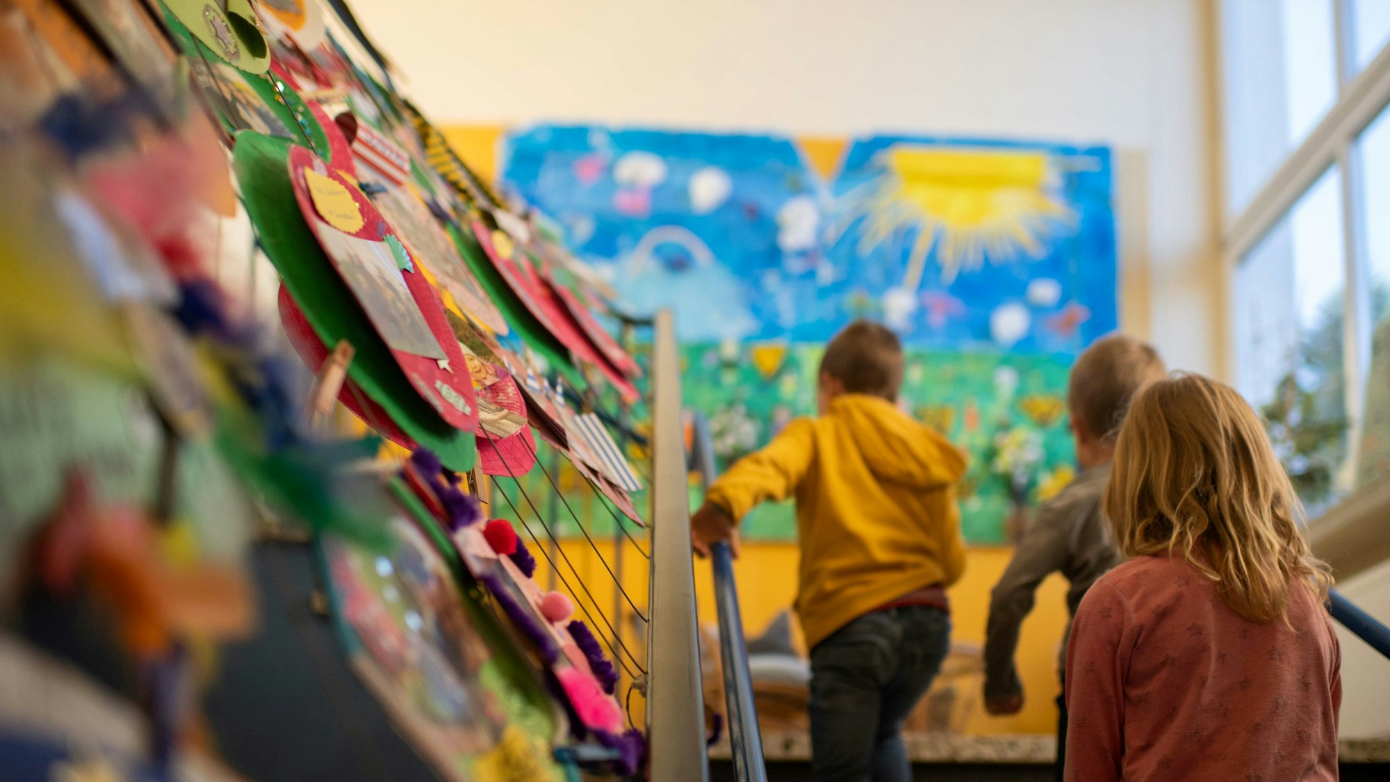 Es ist zu sehen wie drei Kinder in einem Kindergarten eine Treppe hochgehen.