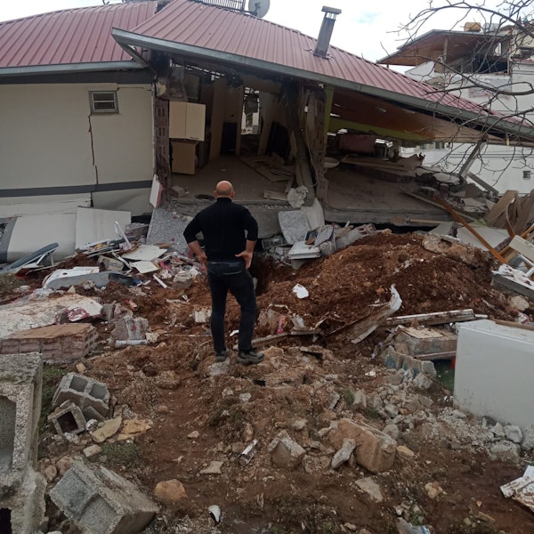 Ein Mann steht vor einem durch das Erdbeben in der Türkei zerstörten Haus.