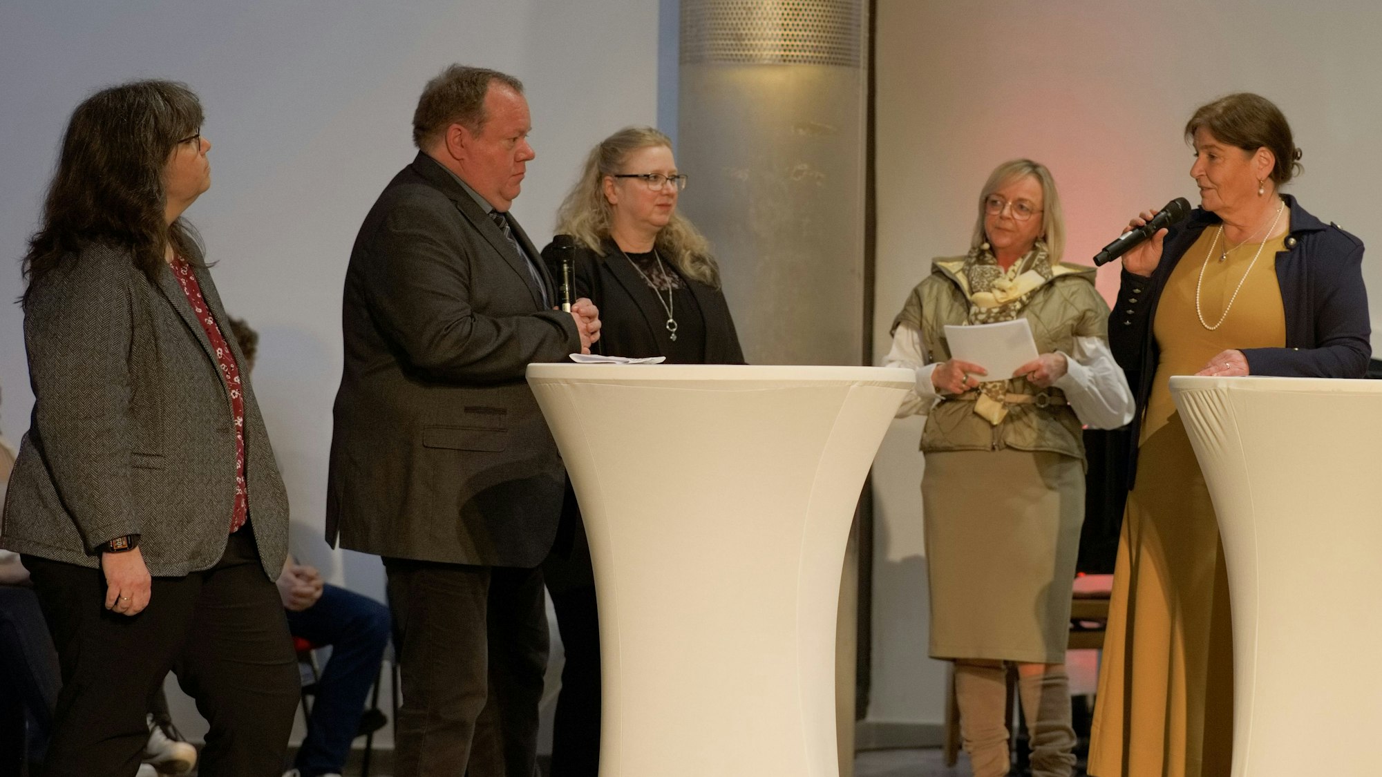 Ein Mann und vier Frauen stehen an Stehtischen.