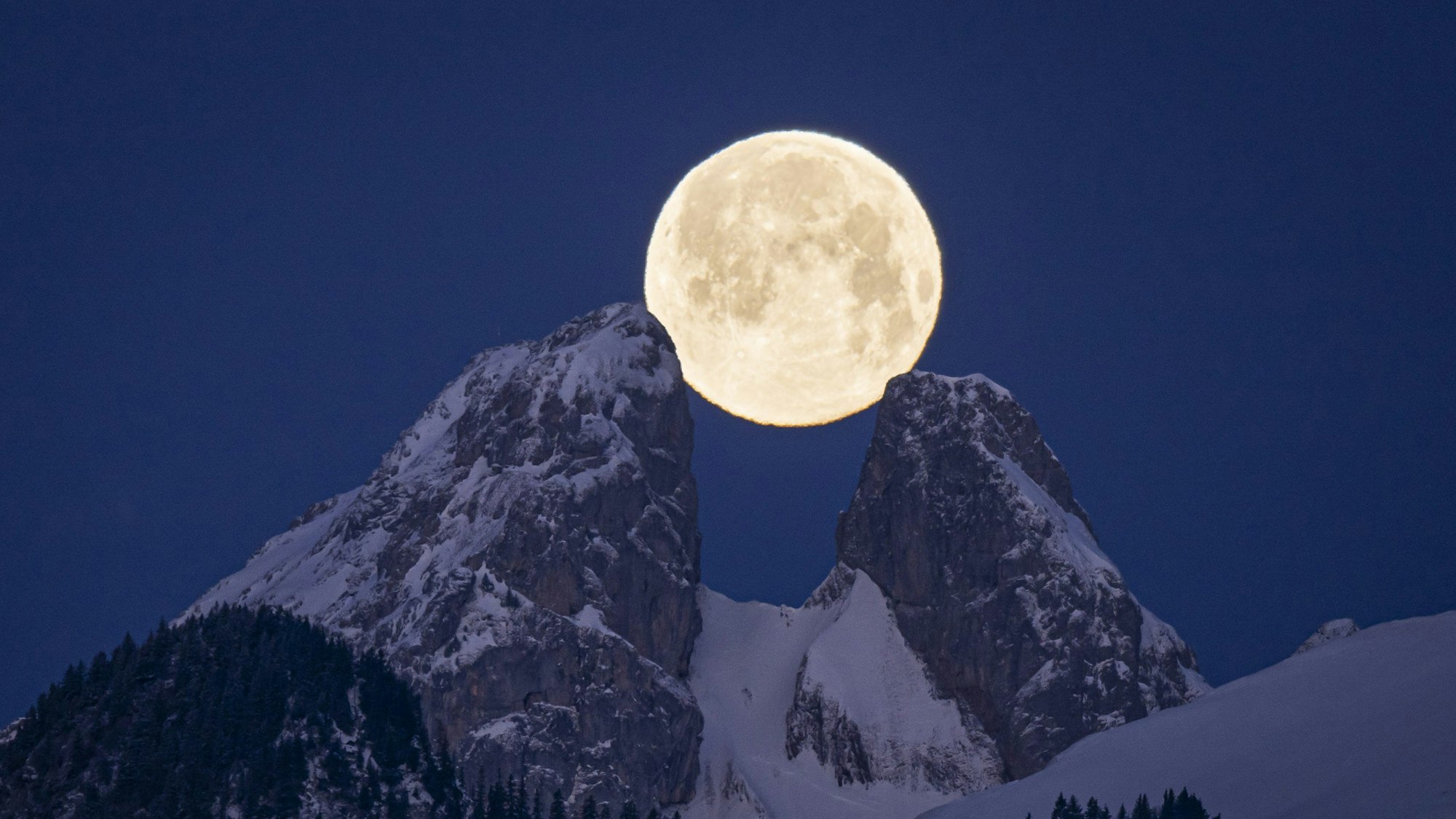 Ein Vollmond, der optisch zwei Bergipfel berührt.