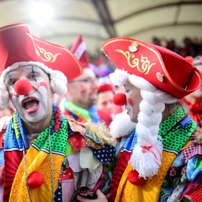 Ein als Clown verkleideter Mann mit roter Pappnase und rotem Hut steht vor der Tribüne am Alter Markt an Weiberfastnacht 2020.