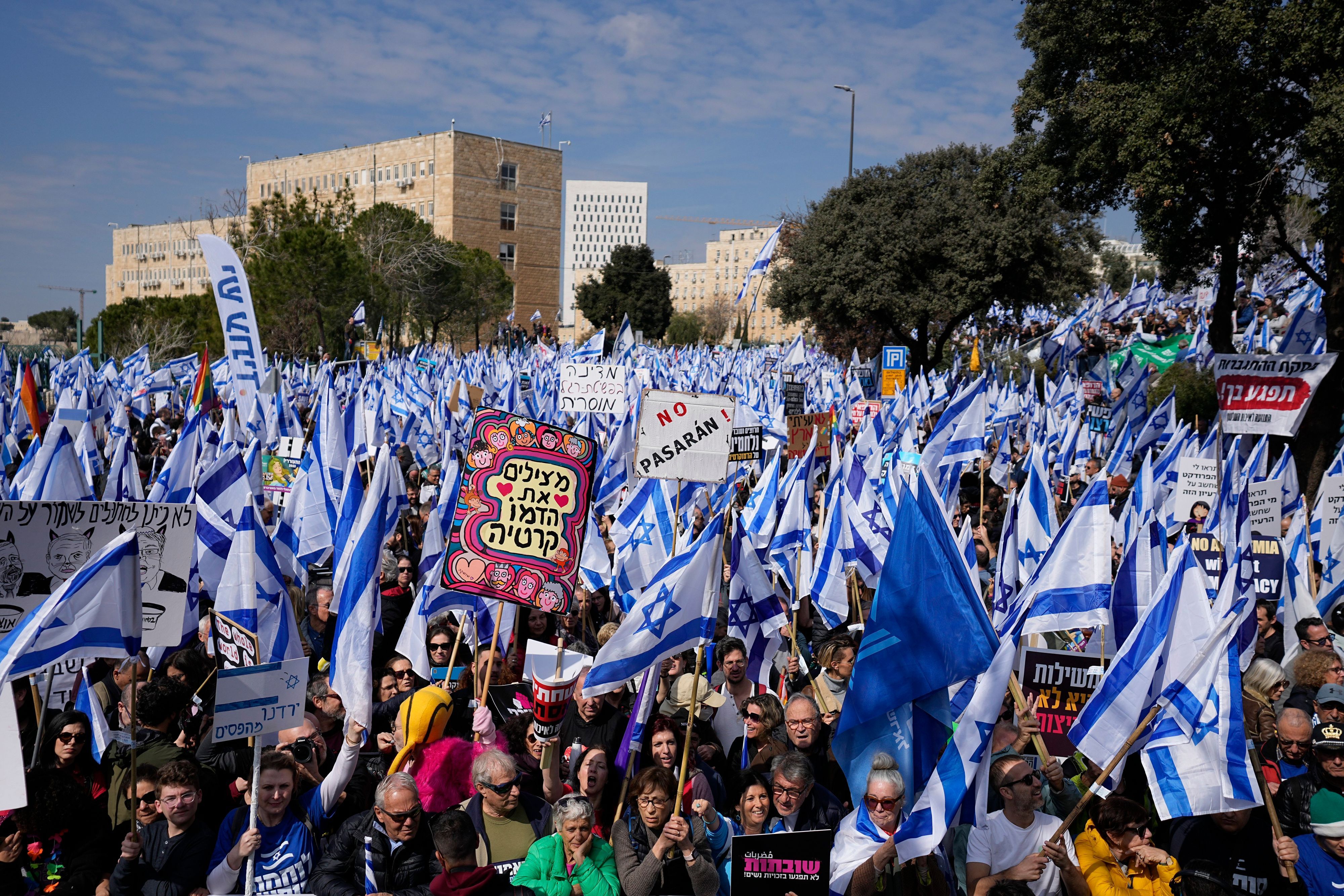Tausende Menschen stehen in Jerusalem vor dem Parlament und halten israelische Flaggen und Protestschilder in die Höhe.