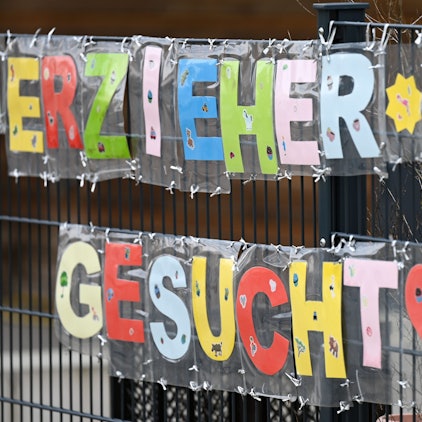 Es sind Schilder mit den Worten „Erzieher*in gesucht“ an einem Zaun beschäftigt.
