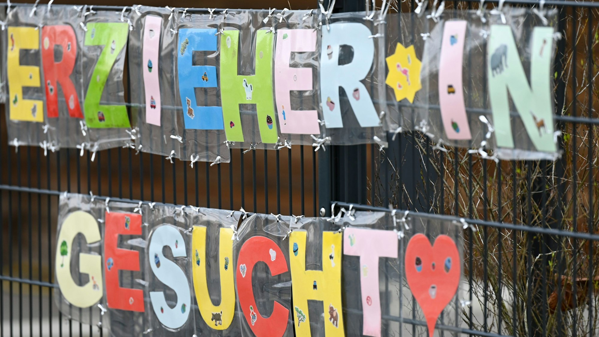 Mit bunten Buchstaben sind die Worte „Erzieher*in gesucht“ geformt, die an einem Zaun einer Kindertagesstätte im Stadtteil Sachsenhausen befestigt sind.