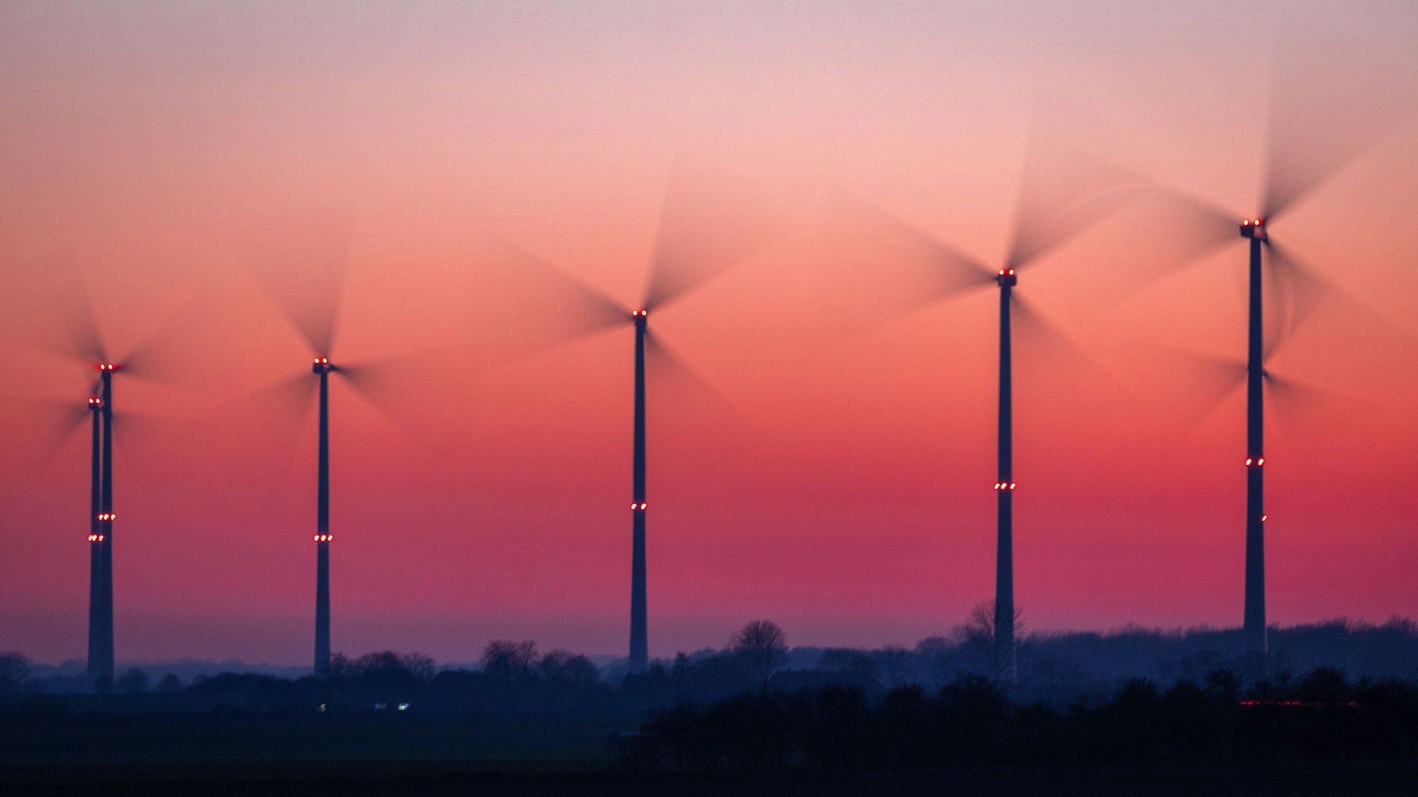 Die Rotoren von Windkraftanlagen drehen sich nach Sonnenuntergang. (Aufnahme mit langer Belichtungszeit)