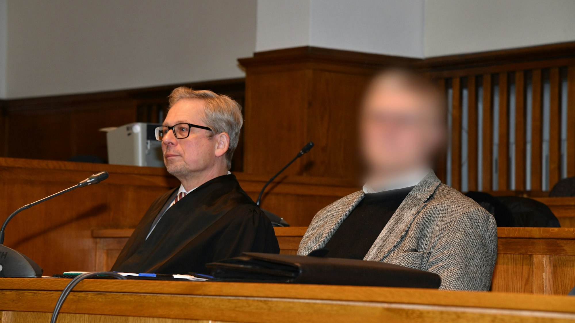 Ein Pfarrer (Gesicht gepixelt) sitzt neben seinem Anwalt im Gerichtssaal.