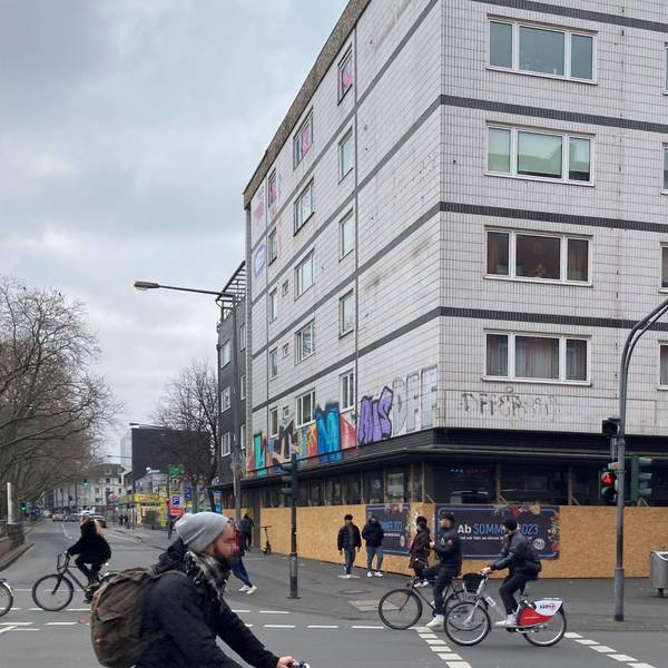 Das Eckhaus der geplanten Aldi-Süd-Filiale ist bisher noch mit Brettern verkleidet, im Vordergrund fahren Fahrradfahrer auf der Straße.