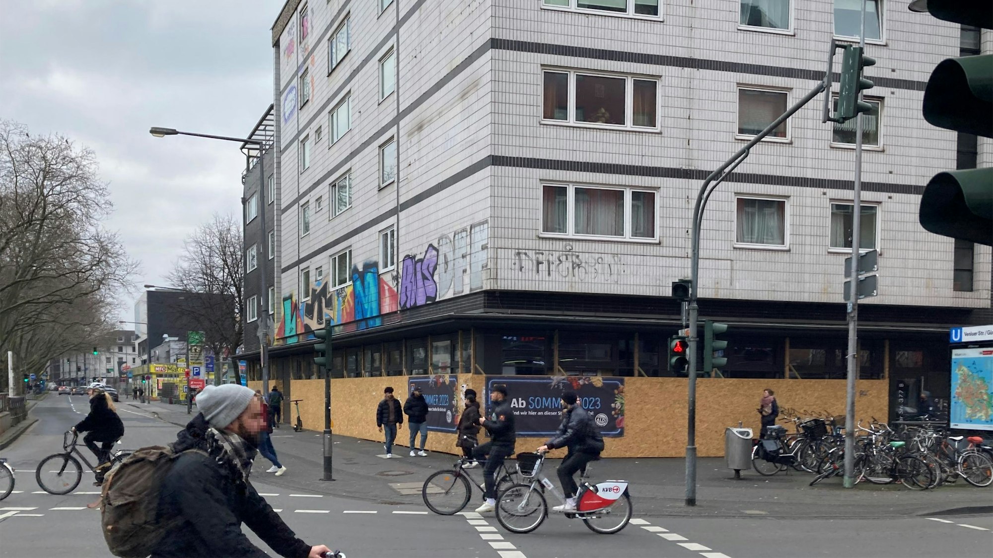 Das Eckhaus der geplanten Aldi-Süd-Filiale ist bisher noch mit Brettern verkleidet, im Vordergrund fahren Fahrradfahrer auf der Straße.