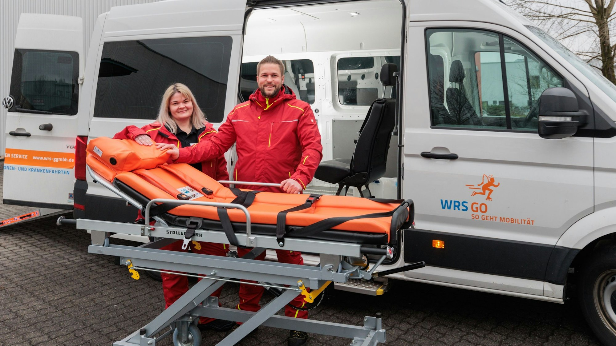 Zwei WRS Go-Mitarbeitende stehen vor einem der Wagen, mit denen Patienten transportiert werden.