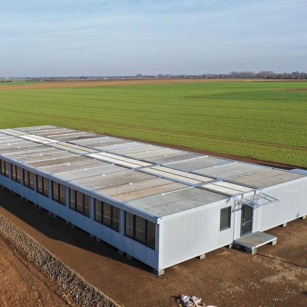 Man sieht einen großen Containerbau, umgeben von Feld.