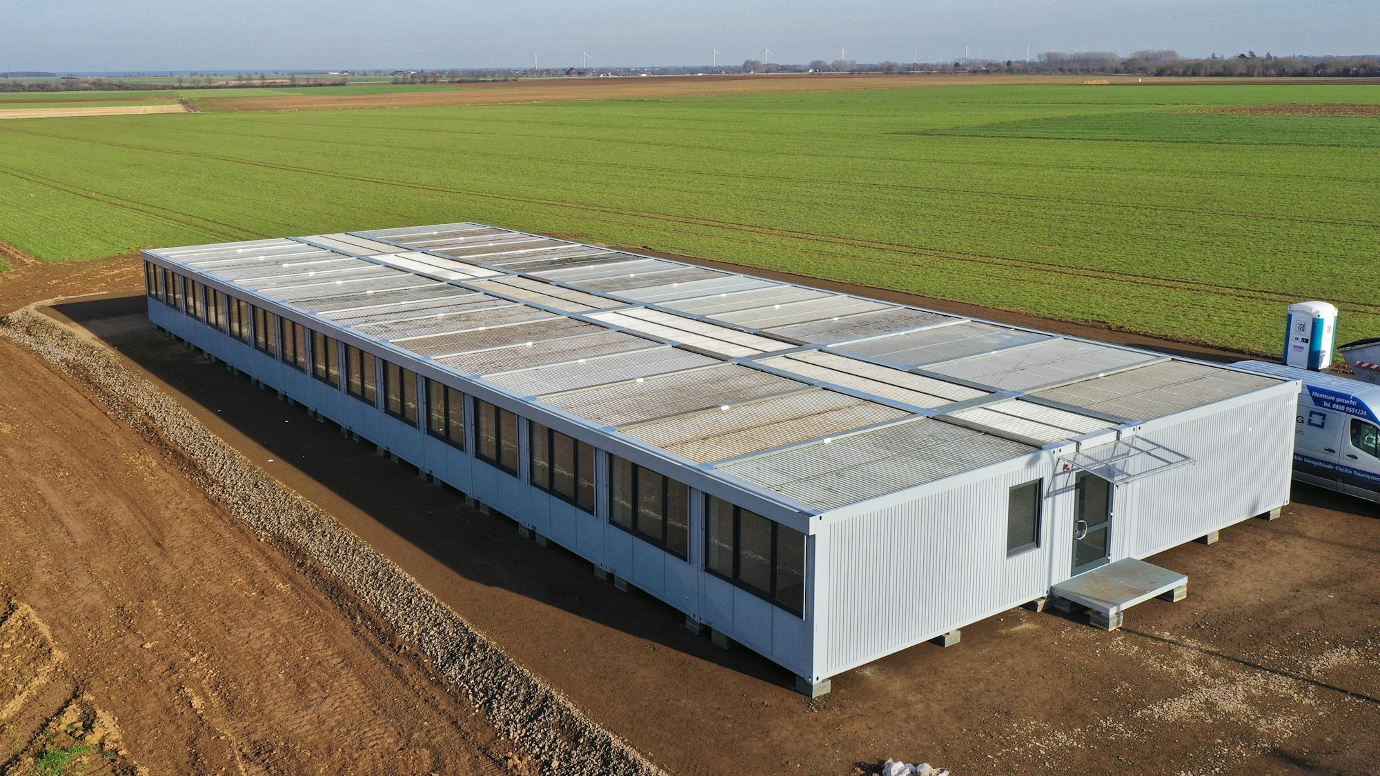 Man sieht einen großen Containerbau, umgeben von Feld.